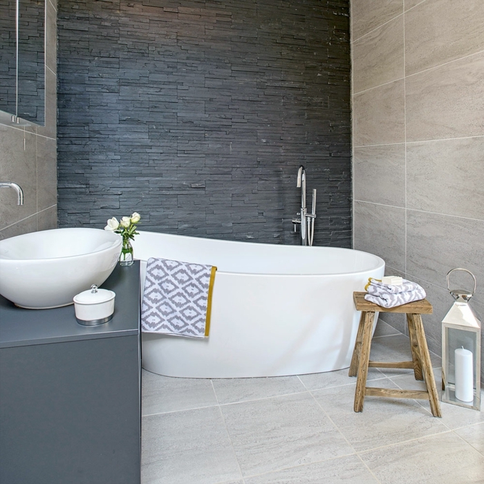 azulejos imitacion madera , bañera blanca con toalla de figuras grises en ella, silla de madera, paredes en gris y beige