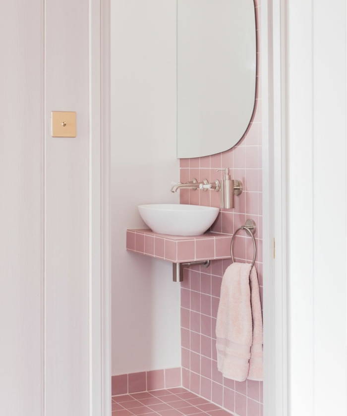 azulejos para baños de color rosa, con toalla rosa, espejo y lavabo pequeño de color blanco