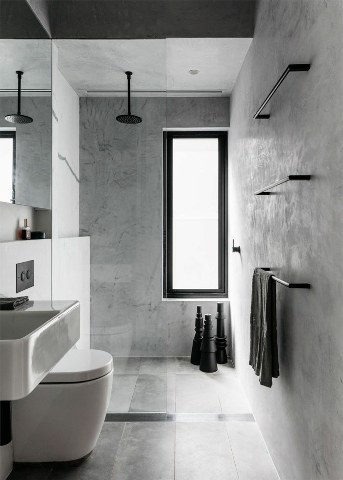 baldosas baño de color gris y negro con ventana larga de color negro, toalla negra, espejo y lavabo blanco