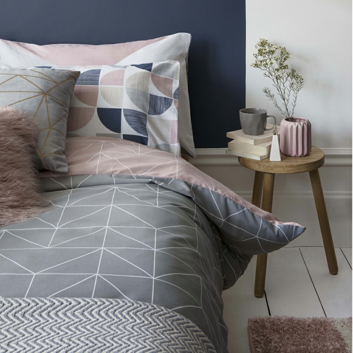 decoracion pisos pequeños, cama con sábanas en gris y rosa con figuras geométricas, mesa de madera