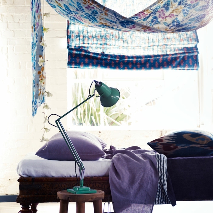 decoracionsalon pequeño, cama con sábanas en lila, lámpara en verde, ventana grande 