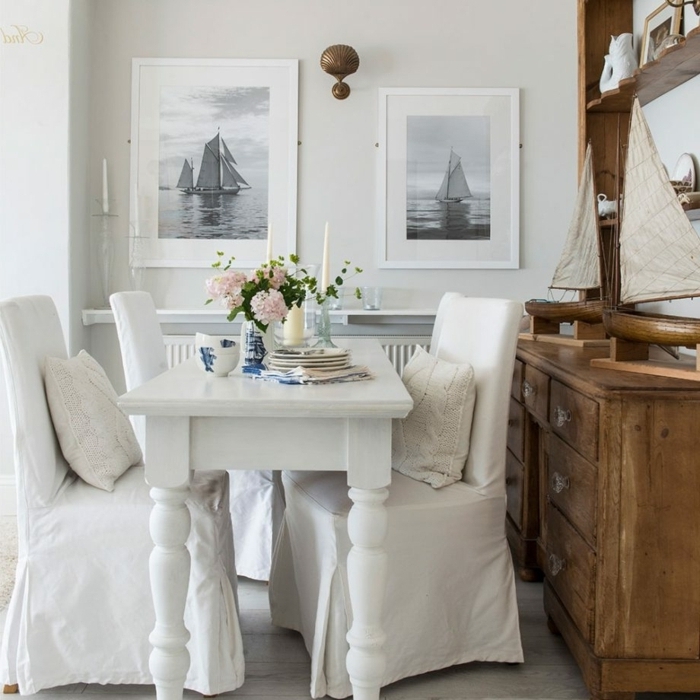 decoracion salon pequeño, mesa de comer blanca con sillas de tela blanca y cuadros de barcos 