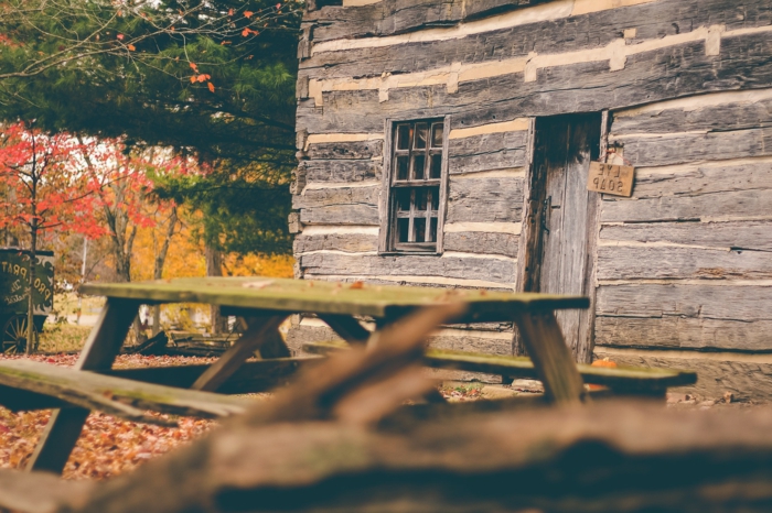 imagenes otoñales, casa de madera con banco con mesa de madera y el suelo lleno de hojas de colores