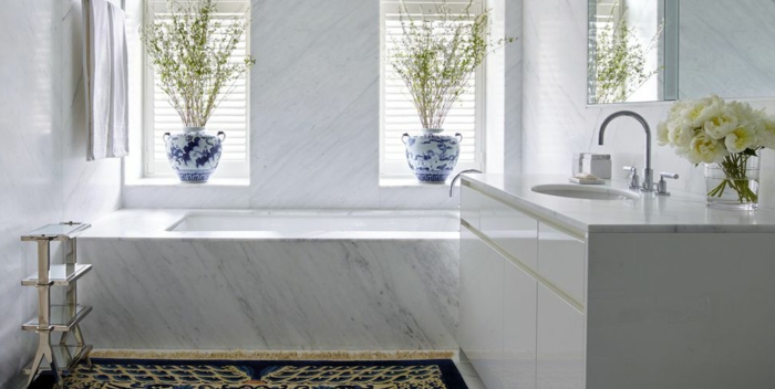 preciosa decoración cuarto de baño blanco, suelo con alfombra, bañera de mármol, decoración de flores 