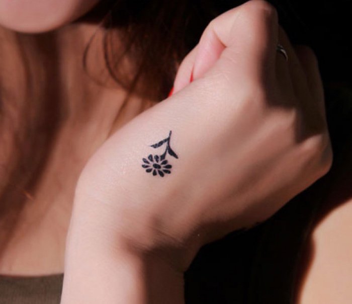ideas de tatuajes pequeños y bonitos en imágines, pequeña flor tatuada en la mano, diseños simbólicos 