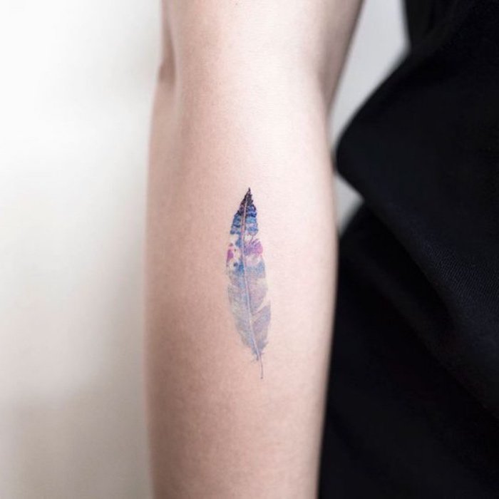 pluma tatuada en el antebrazo en diseño geométrico, pluma en colores pintura acuarela 