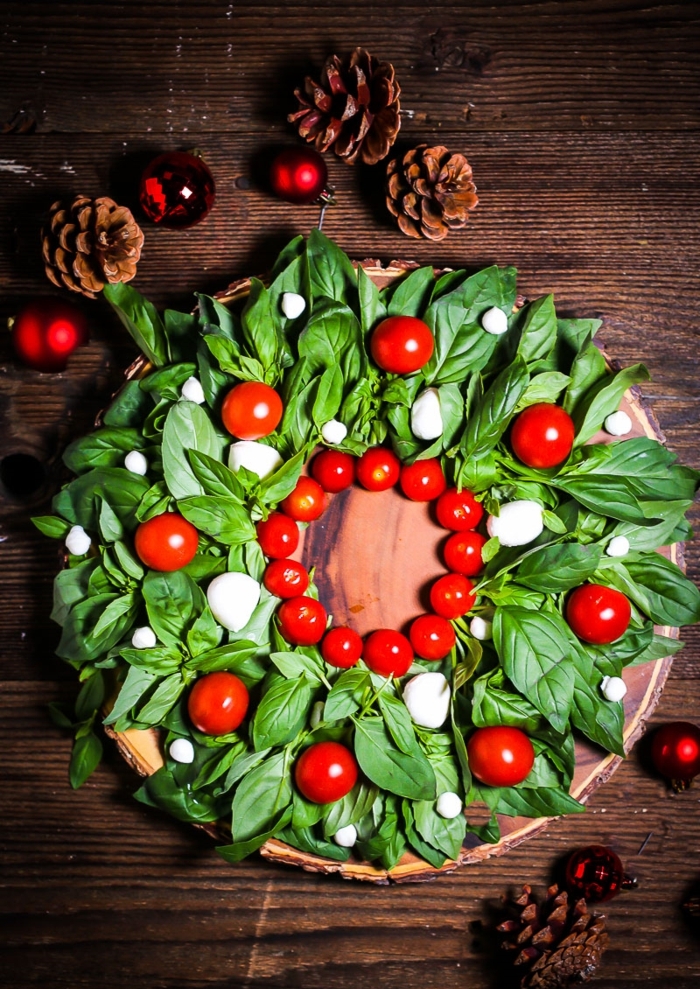 ensalada caprese en forma de corona de navidad, trozos de mozzarella, mini tomates y albahacas frescas, recetas originales con fotos