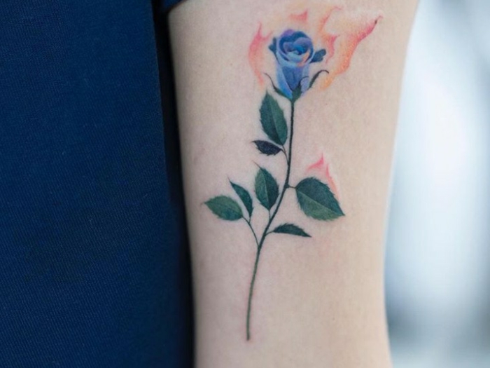 preciosa rosa en color azul tatuada en el brazo, tatuajes simbólicos en el brazo y antebrazo 