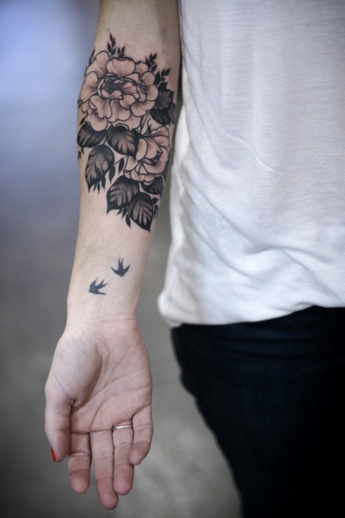 antebrazo tatuado con bonitas rosas en estilo old school en negro, dos aves en pleno vuelo 