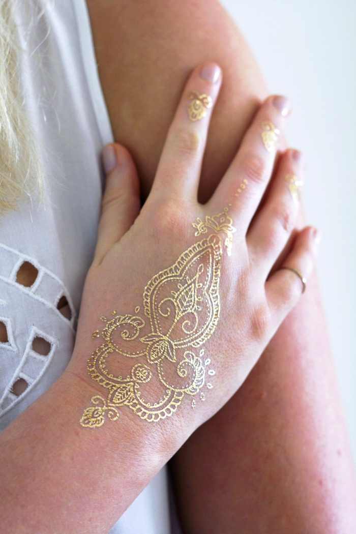 diseños bonitos de tatuajes con henna, mujer con mano tatuada con henna color dorado 