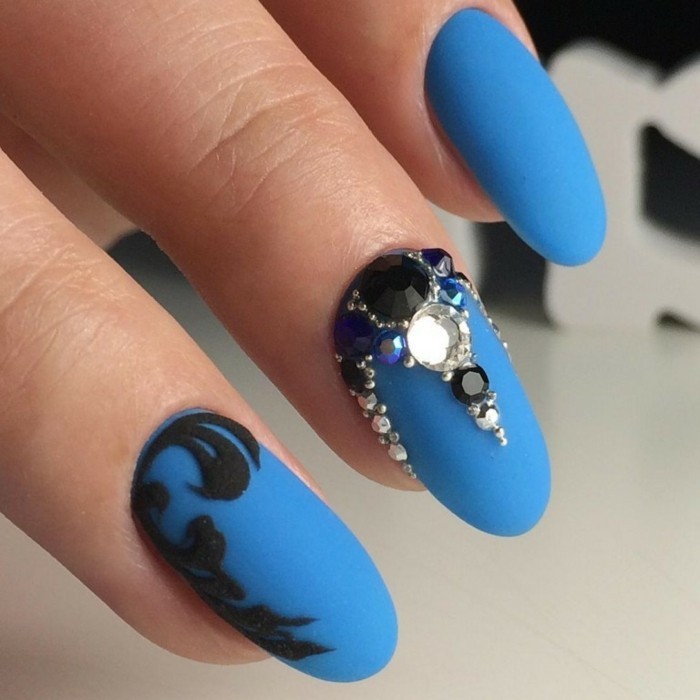 preciosas uñas de forma almendrada pintadas en azul con decoración en negro y cristales brillantes 