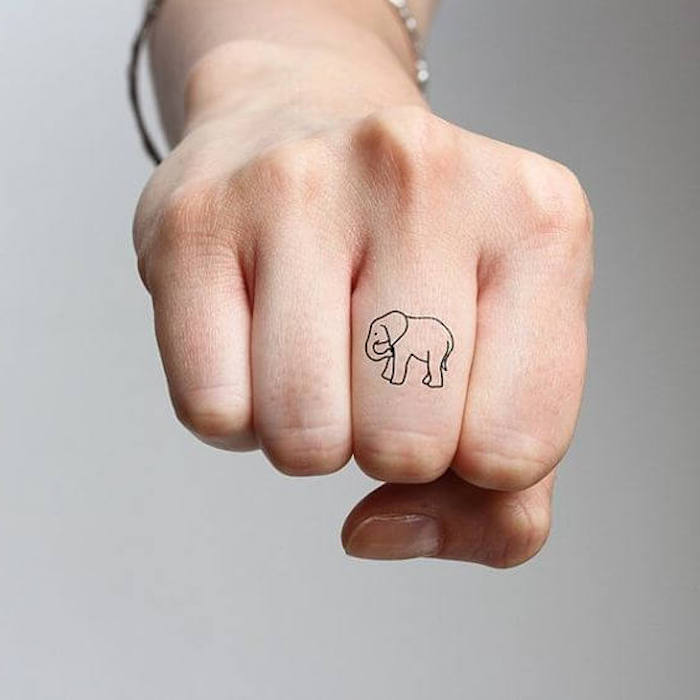 pequeño elefante tatuado en el dedo corazón, tatuajes minimalistas en imagines, diseños originales 