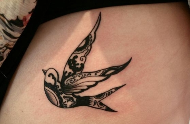 preciosa golondrina tatuada con tinta negra en las costillas, tatuajes con efecto de encaje, significado de los tatuajes con aves 