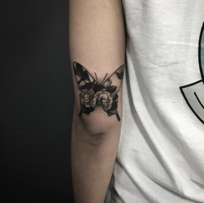 pequeña mariposa tatuada en el brazo, mariposa con flores con tinta negra, diseños de tatuajes que significan cambio y transformación 