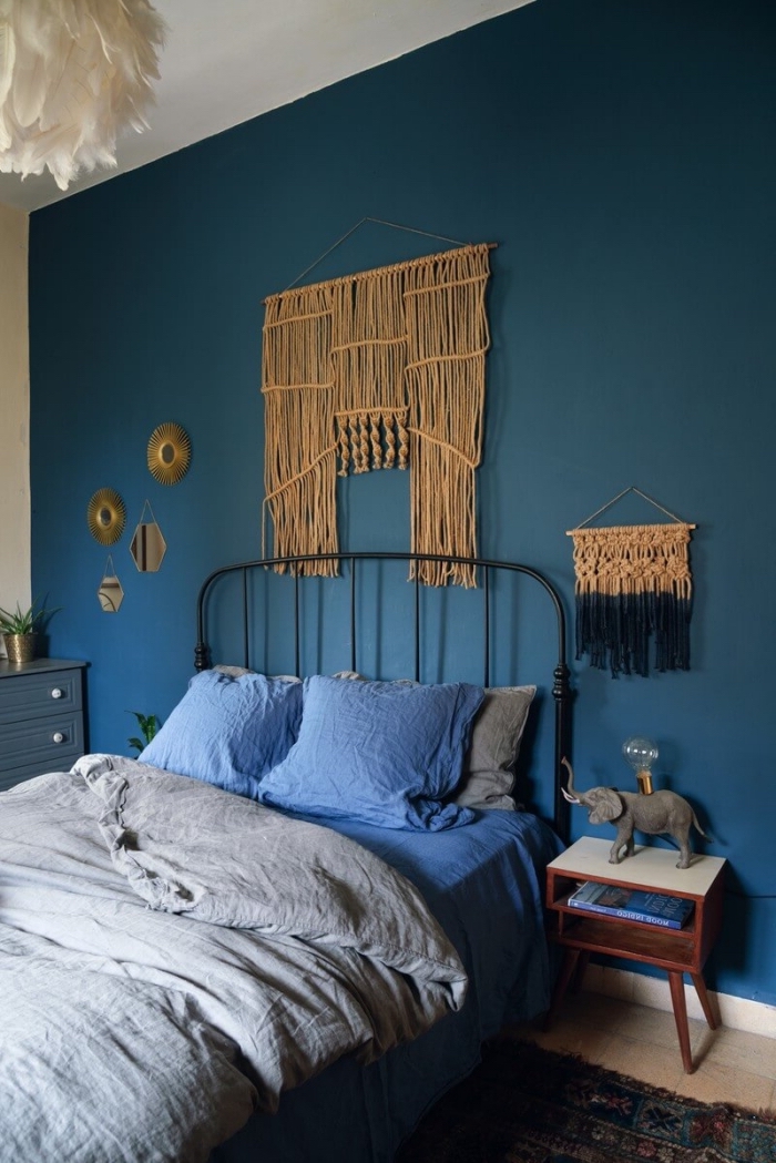 dormitorio decorado en estilo boho chic con paredes en azul intenso, cama doble con cabecero y detalles decorativos en la pared 