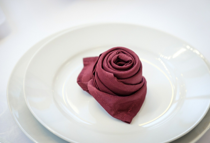 bonitas ideas sobre cómo doblar servilletas de manera elegante, servilleta color berenjena doblada en forma de rosa 