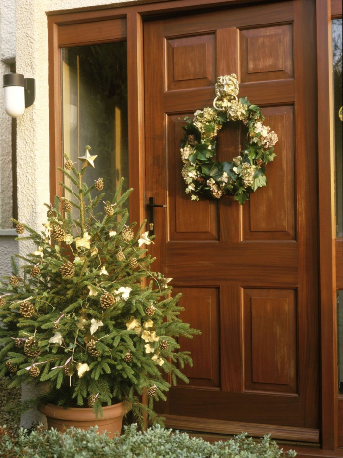 ideas para decorar tu puerta en Navidad, corona verde con detalles en dorado y pequeño árbol navideño, fotos de casas en diciembre 