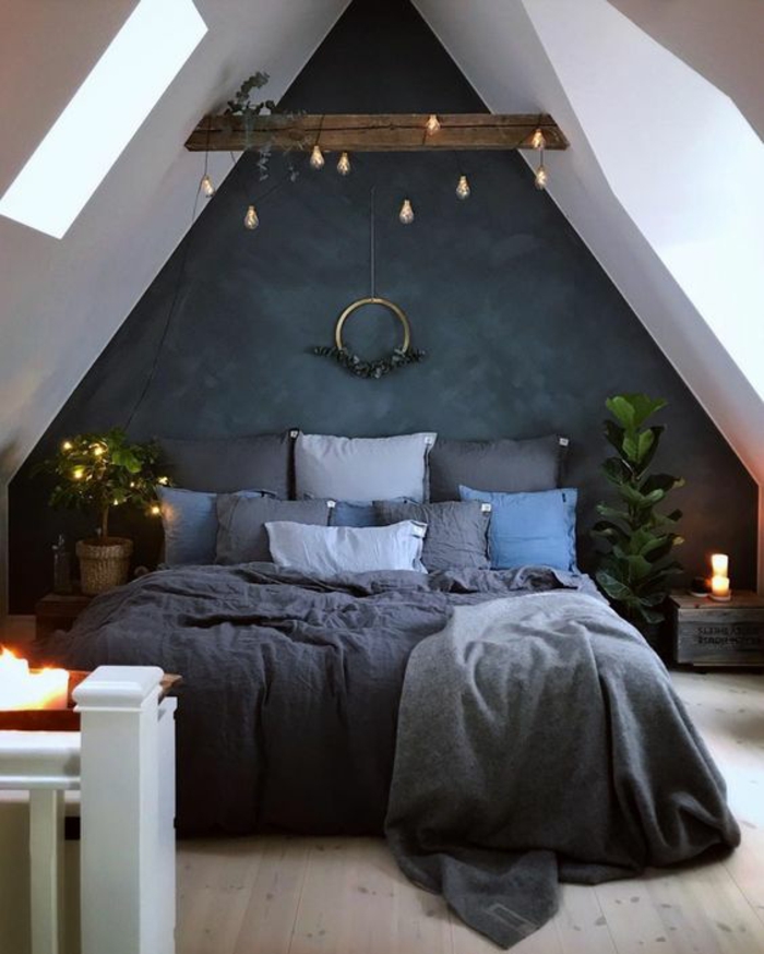 buhardilla decorada en tonos oscuros, techo abuhardillado pintado en blanco, cama doble con almohadas en diferentes colores 
