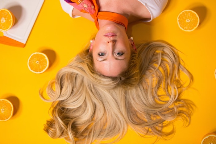 mujer joven con cabello rubio hombros largos acostada sobre un fondo naranja
