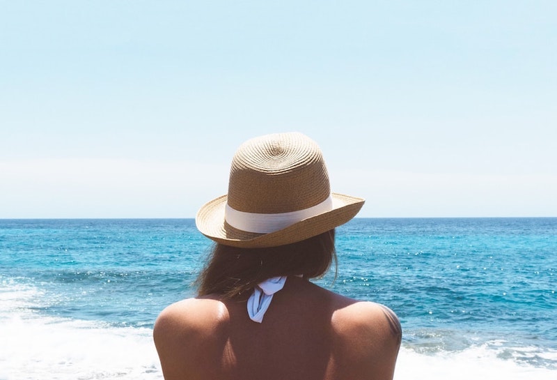 mujer sentada en la playa en la espalda sombrero de paja
