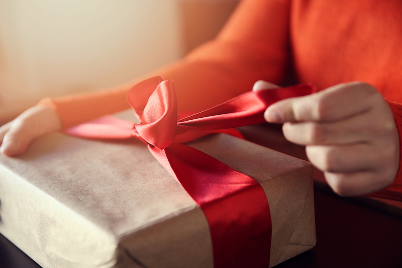 hand pulls red ribbon on a gift wrapped in brown paper