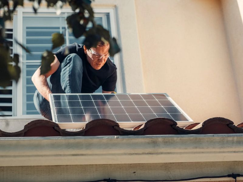 un hombre instalando un panel solar en el techo de una casa