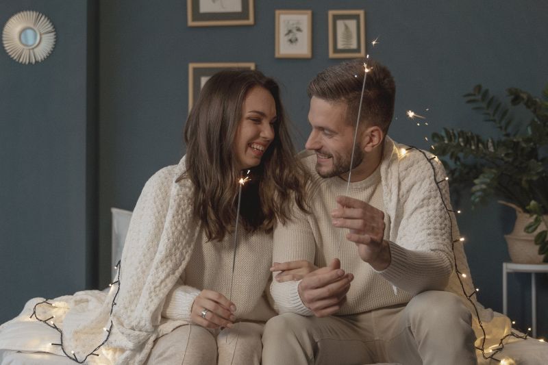 pareja feliz con luces navideñas sentada en el sofá en la sala de estar