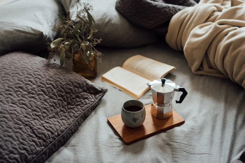 cama con mantas grises con cafetera y libro
