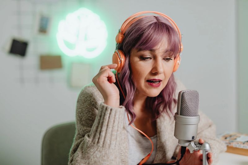 una mujer con el pelo rosa y auriculares naranjas haciendo un podcast