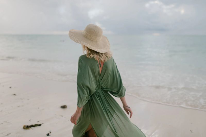 chica rubia caminando por la playa con vestido verde y sombrero