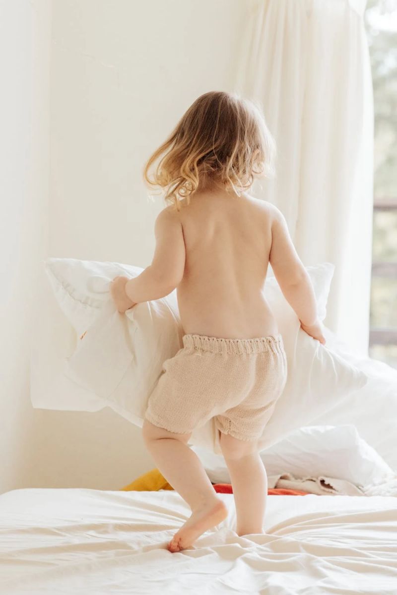 un bebé con pantalones beige saltando sobre una cama con sábanas blancas