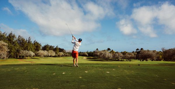 hombre con camiseta blanca y pantalón corto naranja jugando al golf